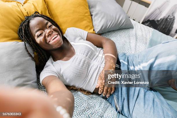 happy millennial african woman taking selfie with smartphone app while relaxing on bed. - interface dots stock pictures, royalty-free photos & images