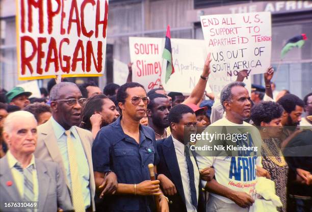 View of American tennis player Arthur Ashe and singer Harry Belafonte , among others, as they march during a demonstration outside the United...