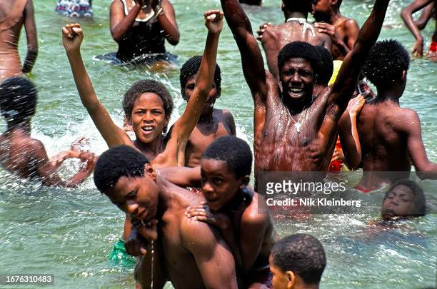 View of people as they play in the water of the Astoria Public Pool in Queens, New York, New York, summer 1983.