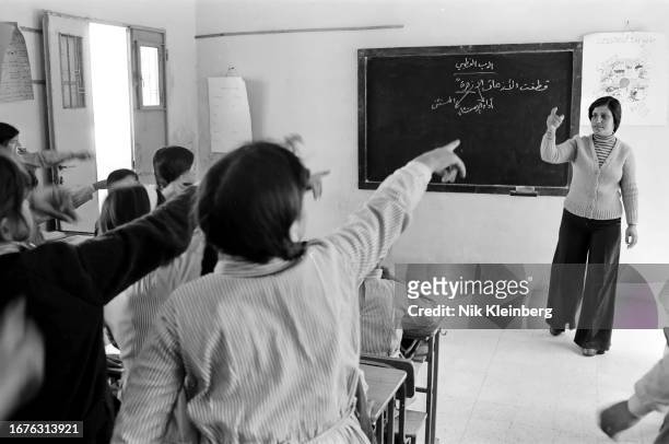 Teacher leads a classroom of students, many of whom stand with their arms outstretched, Beit Fajjar, West Bank, April 1978.