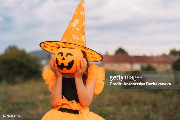 a child in an orange witch costume hides her face behind a pumpkin-shaped bucket - halloweenlykta bildbanksfoton och bilder