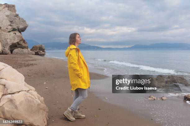 lonely on the beach on gloomy day. thoughtful mature woman (40-49 years) spending time alone on empty autumn beach and watching the grey tranquil sea - 40 49 years ストックフォトと画像