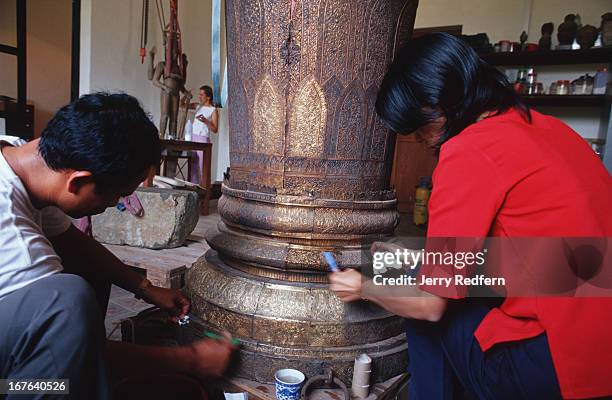 National Museum technician Thlang Sakhoeun, in red, works with another museum employee to restore a royal funeral urn discolored and filled with...