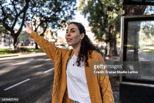 young woman hailing a taxi/bus in the bus stop - uber in buenos aires argentina stock pictures, royalty-free photos & images
