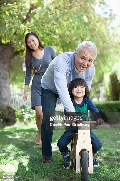 older man pushing grandson in backyard - seniors having fun with grandson stockfoto's en -beelden