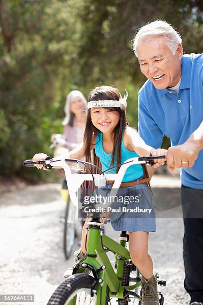 ältere mann helfen enkelin reiten fahrrad - fahrrad fahren großeltern mit kind stock-fotos und bilder