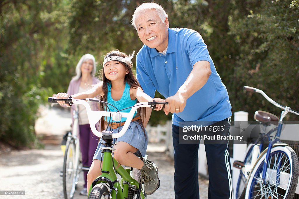 Older man helping granddaughter ride bicycle