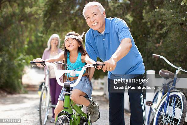 older man helping granddaughter ride bicycle - asian cycling stock pictures, royalty-free photos & images