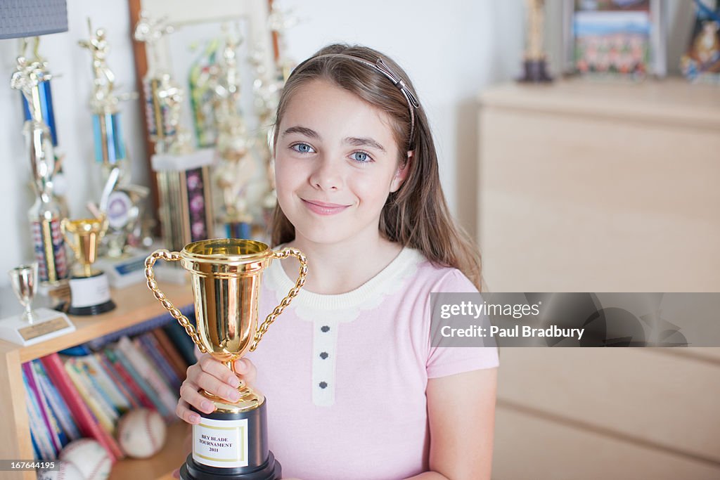 Smiling girl holding trophy in bedroom