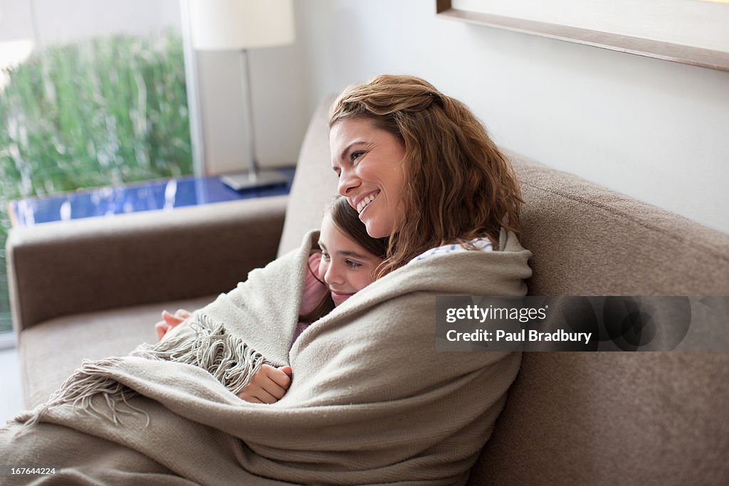 Mother and daughter wrapped in blanket on couch