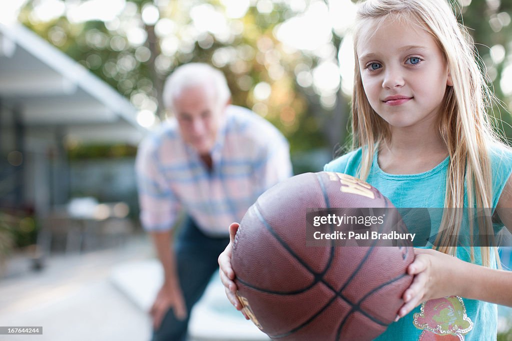 Older man playing basketball with granddaughter