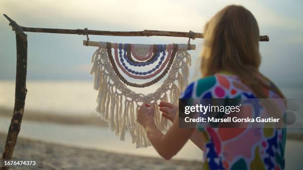 a woman weaves macrame on the beach at sunset. - macrame stock pictures, royalty-free photos & images