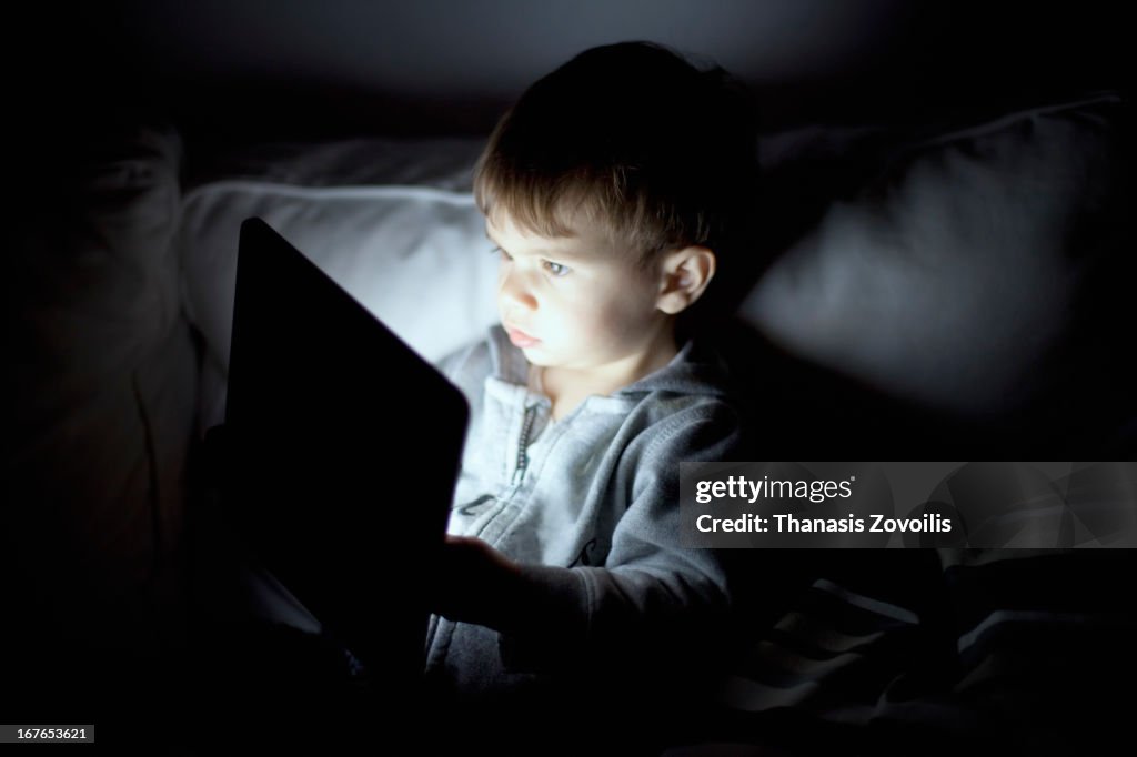 Small boy looking at a tablet in the dark