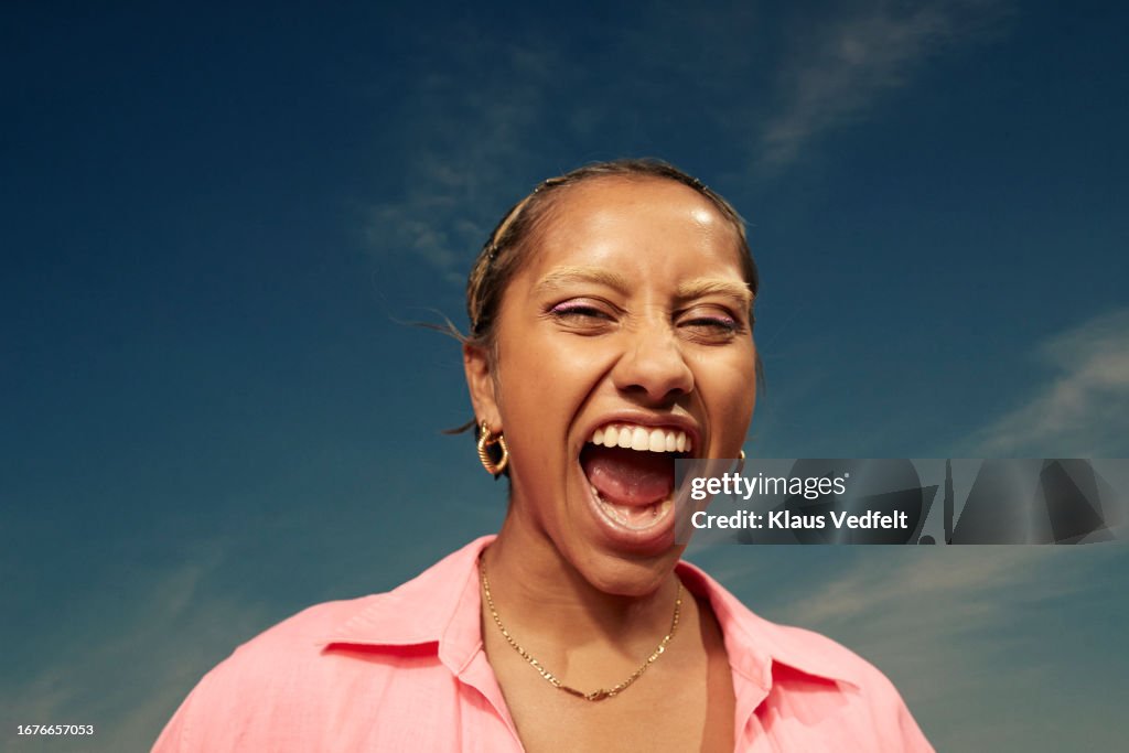 Woman opening mouth and screaming against sky