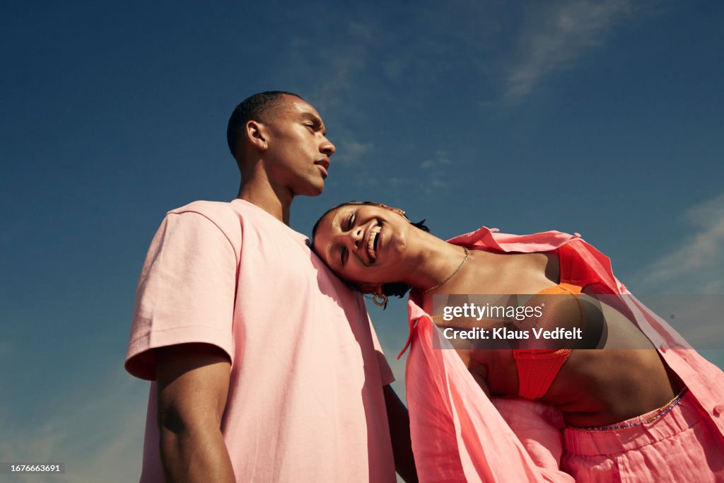 Smiling woman leaning on man against sky