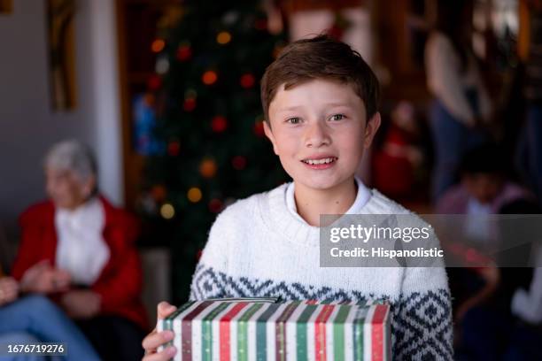 porträt eines schönen 10-jährigen jungen, der ein weihnachtsgeschenk hält, während er lächelnd in die kamera blickt - 20 year old stock-fotos und bilder