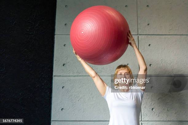 slender mature woman doing exercise with fitness ball - pilates for active retirees - fitness ball stock pictures, royalty-free photos & images