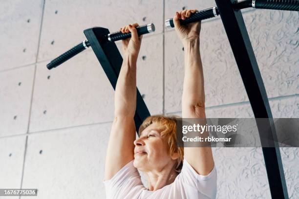 mature woman hanging on the horizontal bar in the gym - gymnastics bar stock pictures, royalty-free photos & images