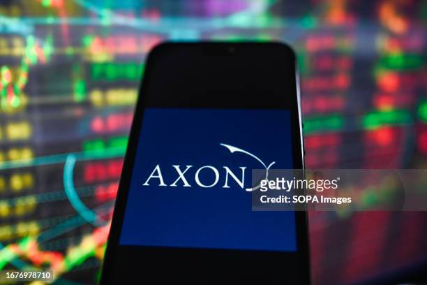 In this photo illustration, a Axon logo seen displayed on a smartphone with stock market percentages in the background.