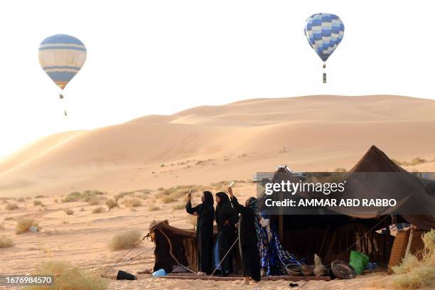 Tuaregs women of nomadic tribes take pictures with their mobile phones of hot air balloons flying over the desert of Ghadames, western Libya, on...