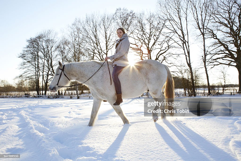 Young woman riding a white horse in the snow