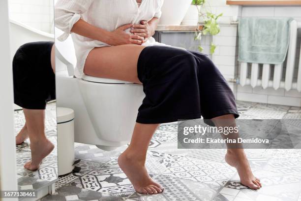 unrecognizable woman holds her hands on her stomach, twisted in pain in toilet - emorroidi foto e immagini stock