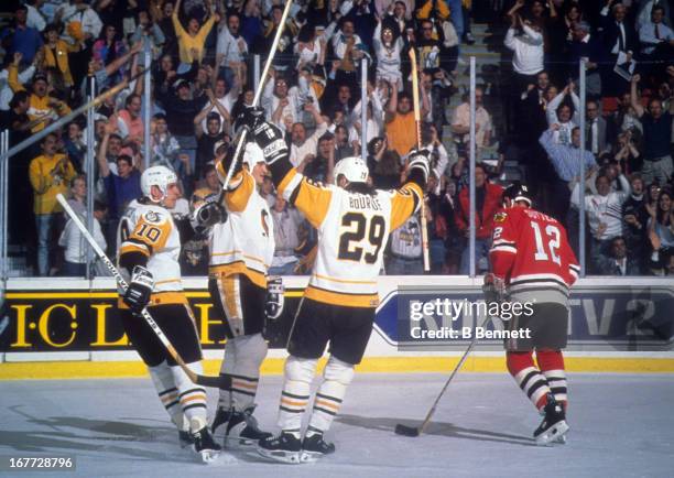 Mario Lemieux of the Pittsburgh Penguins celebrates with teammates Ron Francis and Phil Bourque as Brent Sutter of the Chicago Blackhawks skates by...