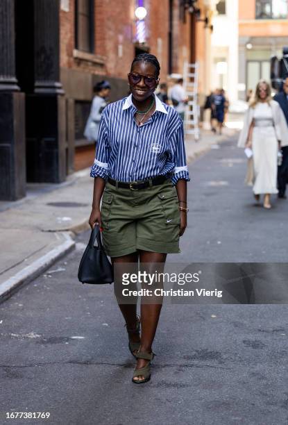 Guest wears blue white stripped button shirt, green shorts, black bag outside Brandon Maxwell on September 12, 2023 in New York City.