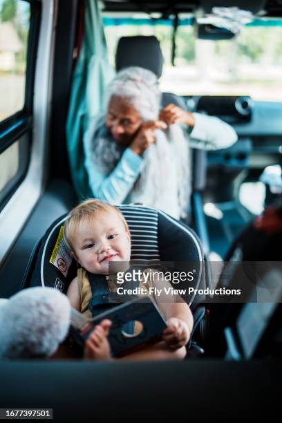 かわいい1歳の子供がチャイルドシートに座りながら絵本を持つ - 65 year old asian women ストックフォトと画像