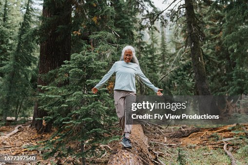 Active senior woman balances on fallen tree Active senior woman balances on fallen tree
