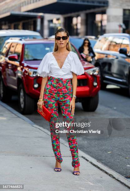 Guest wears white blouse, red pants with floral print outside Carolina Herrera on September 12, 2023 in New York City.