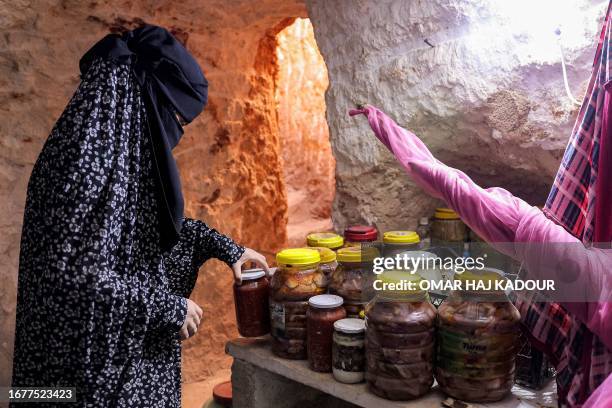 Member of Ahmad Khalil's family arranges jars of food in a cave he carved manually with his children in five years, near his original home in the...