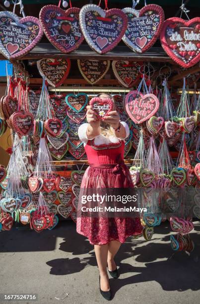 blonde woman in dirndl dress buying gingerbread heart souvenir at german beer festival - dirndl stock pictures, royalty-free photos & images