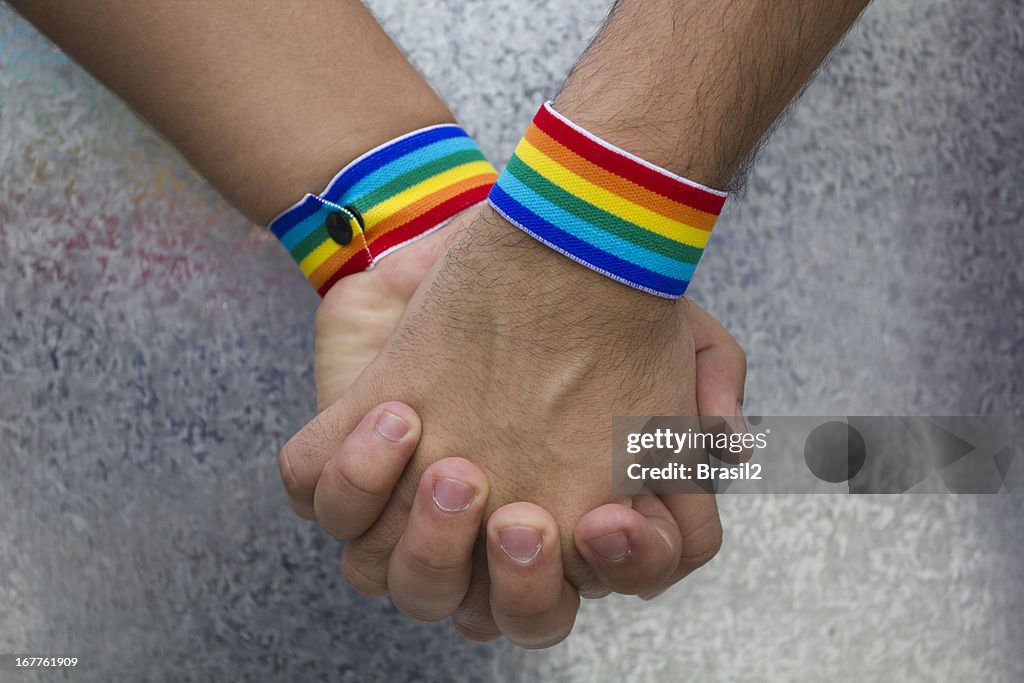 Two people holding hands and wearing rainbow bracelets