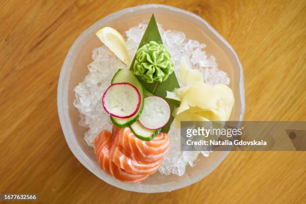 sushi and vegetables in ice cube on plate in restaurant. on ice are slices of salmon, radish and cucumber, wasabi and ginger. top view - fresh wasabi stockfoto's en -beelden