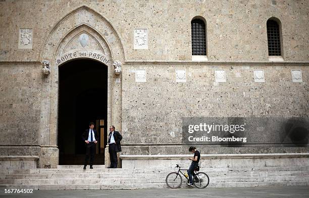 Pedestrians and a bicyclist stand outside the headquarters of Banca Monte dei Paschi di Siena SpA in Siena, Italy, on Monday, April 29, 2013. An...
