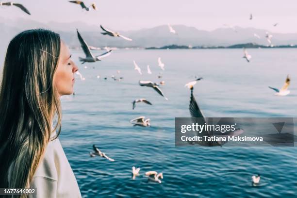 a young woman with long hair stands with her eyes closed, a flock of seagulls flies against the backdrop of the sea. - turkey feathers stock pictures, royalty-free photos & images