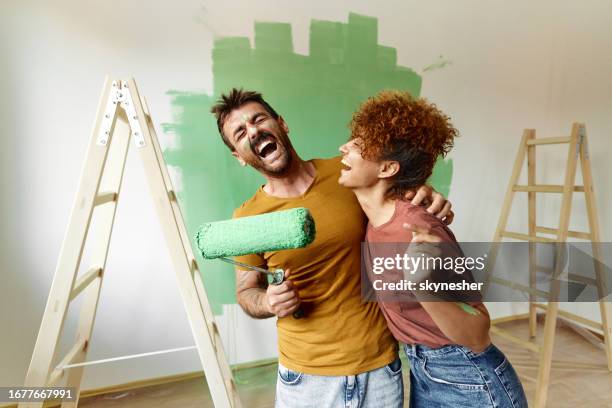 cheerful couple having fun while painting their new apartment in green. - home improvement stock pictures, royalty-free photos & images