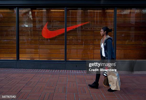 Woman carries a shopping bag while passing in front of a Nike Inc. Store in Portland, Oregon, U.S., on Wednesday, April 24, 2013. The U.S. Conference...