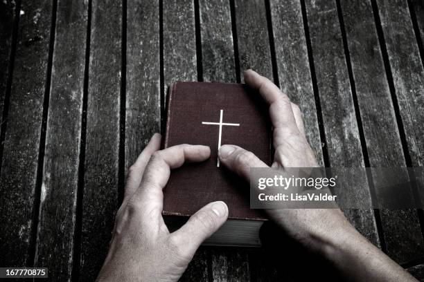 hands holding a bible atop a dark wooden surface - bible stock pictures, royalty-free photos & images