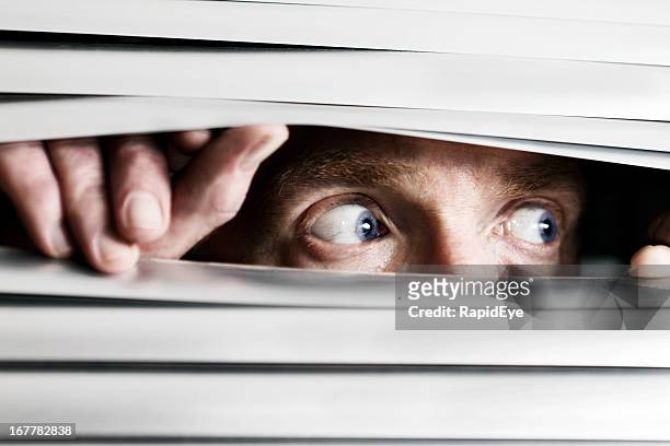 fearful man looking sideways through venetian blind - nosy stock pictures, royalty-free photos & images
