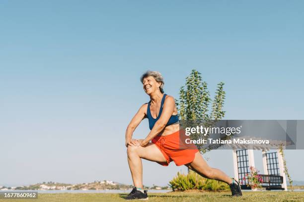 senior gray-haired woman doing exercises in public park, sunny summer morning. - gray shorts stock pictures, royalty-free photos & images