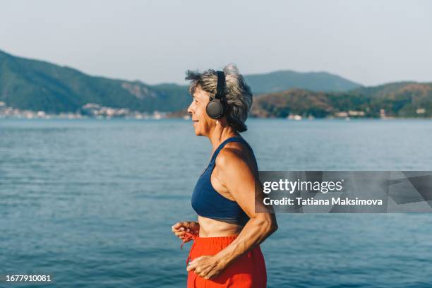 senior woman in headphones runs in park, sunny summer day. - one embankment stock pictures, royalty-free photos & images