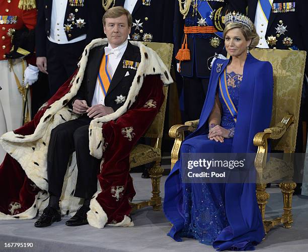 King Willem Alexander of the Netherlands and HM Queen Maxima of the Netherlands sit on their thrones in front of members of the royal household...