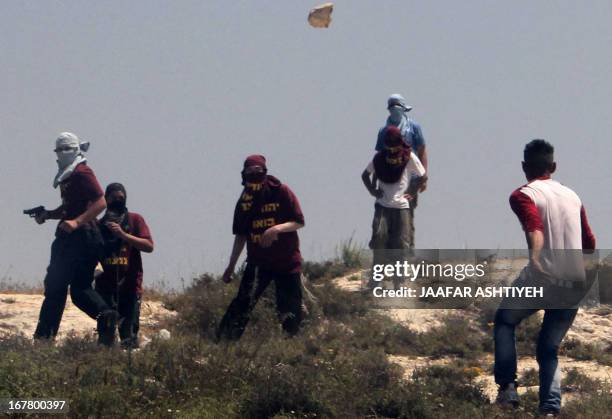 Masked Israeli settler holds a gun as others throw stones towards a Palestinian youth during clashes in the West Bank village of Urif, near Nablus,...