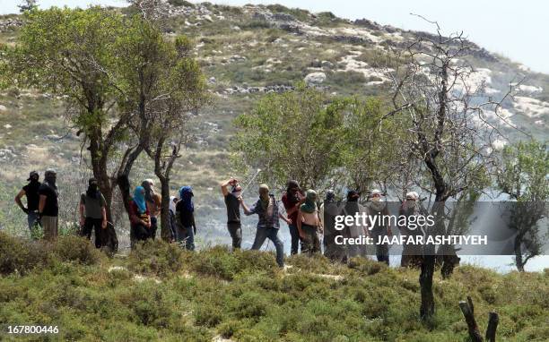 Masked Israeli settlers throw stones towards Palestinians in the West Bank village of Urif, near Nablus, on April 30, 2013 during clashes after an...