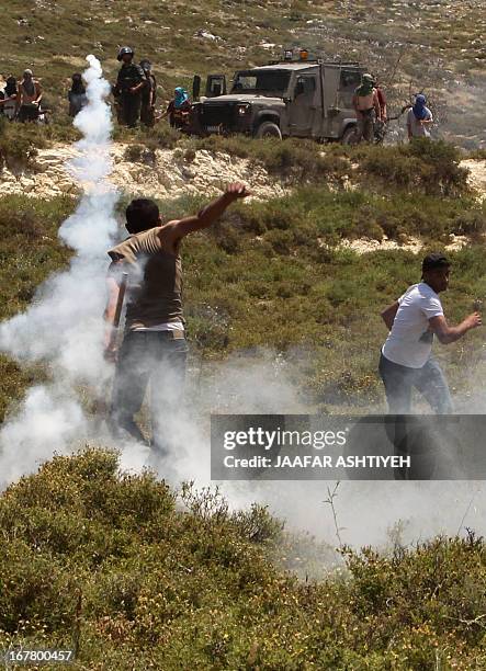 Palestinian man throws back a tear gas canister towards masked Israeli settlers and members of the Israeli security forces during clashes in the West...