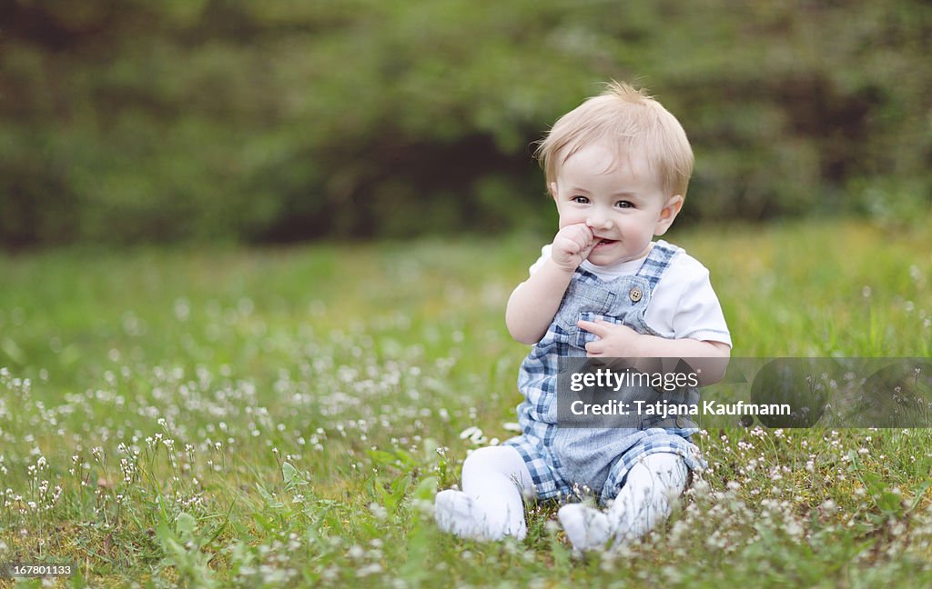 Cute Baby Boy sitting in Grass in Spring, smiling