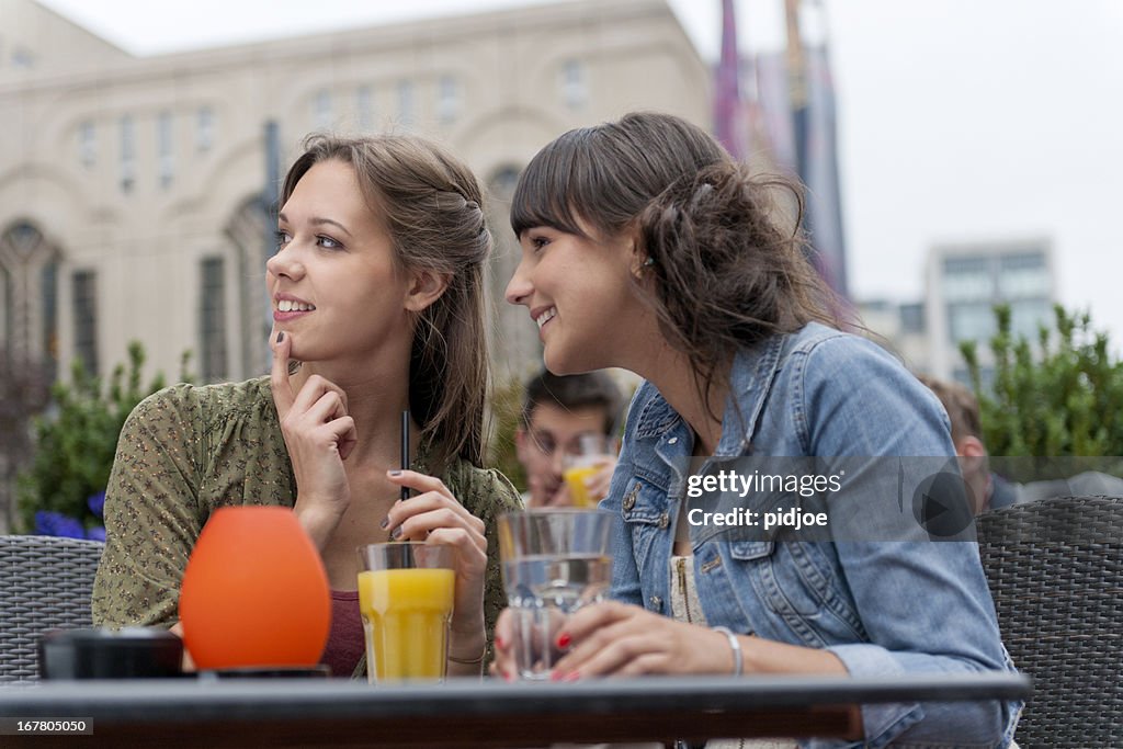 Flirting young women sitting at sidewalk cafe