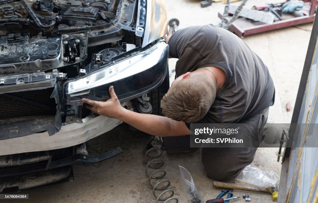 Young auto mechanic is repairing a car headlight.
